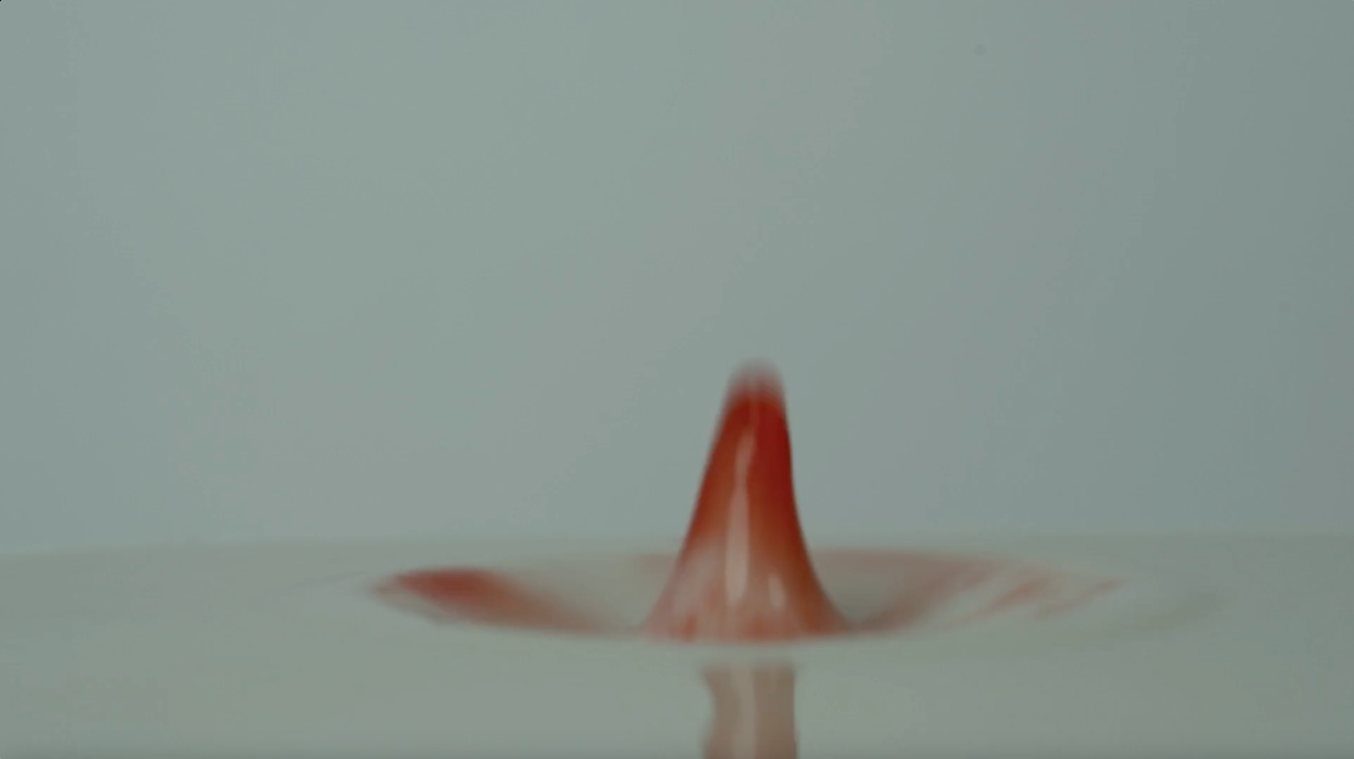A red drop rises from the surface of pale liquid.