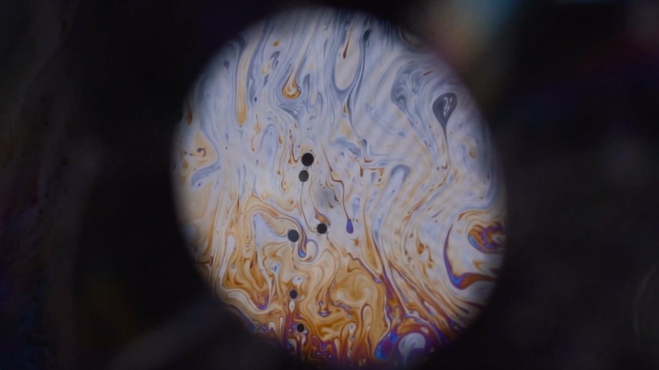 A soap film seen through a round lens, swirling with interference colors.